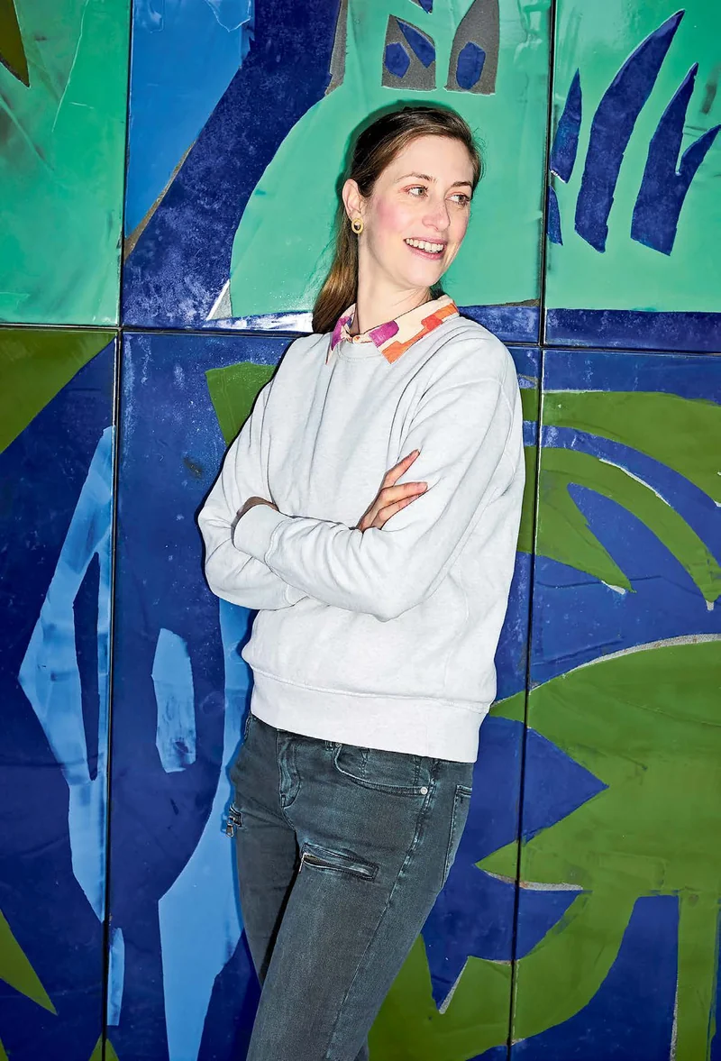 Andrea Horka lächelt vor einer grün-blauen Wand.